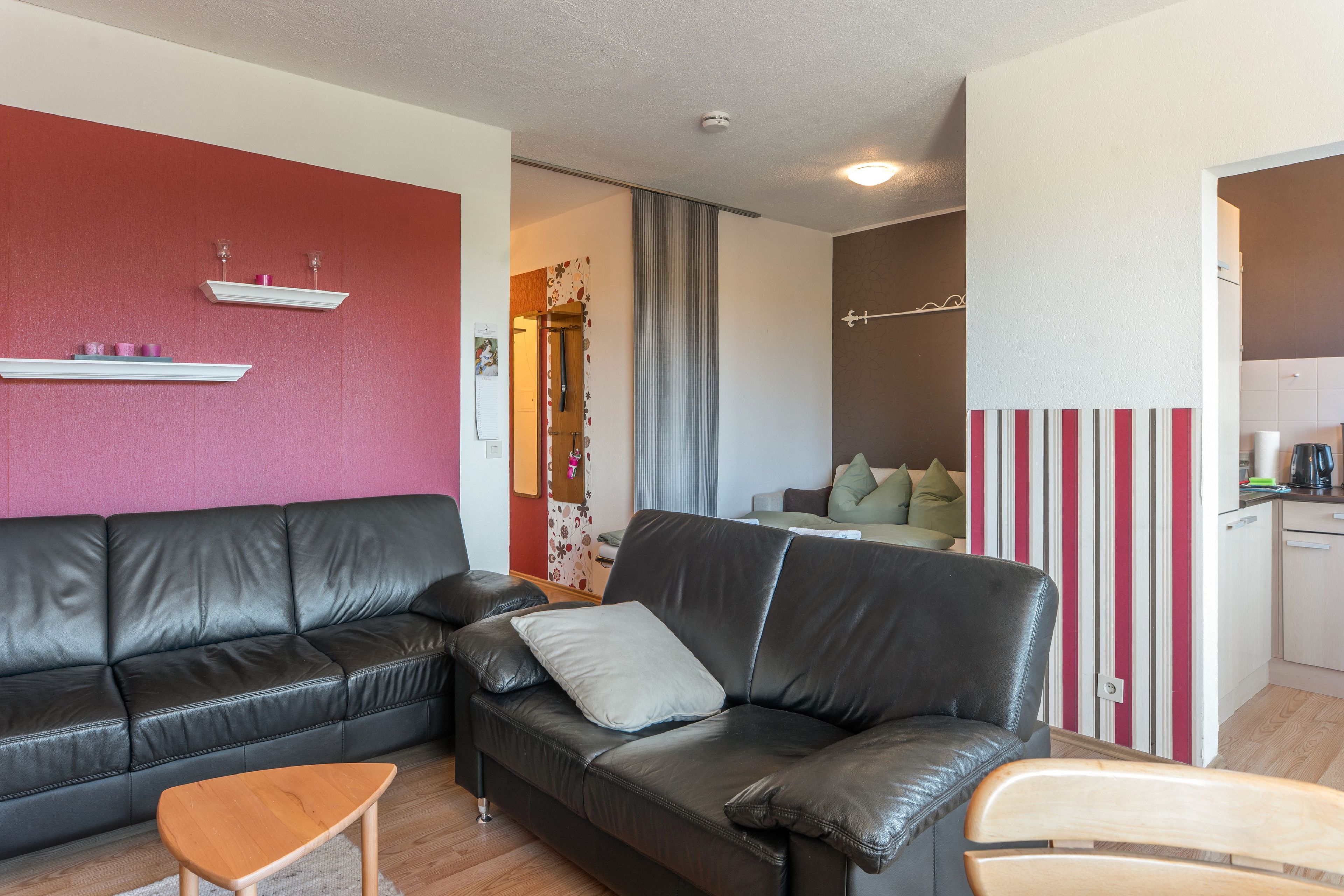 A modern living room with a black leather sofa, a wooden coffee table, and a striped accent wall.