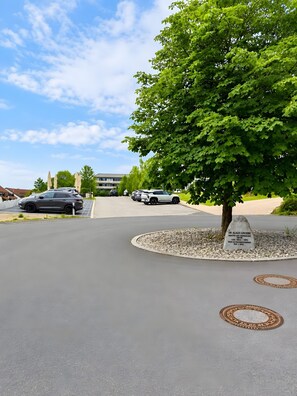 A parking area with a tree, a manhole cover, and a building in the background.