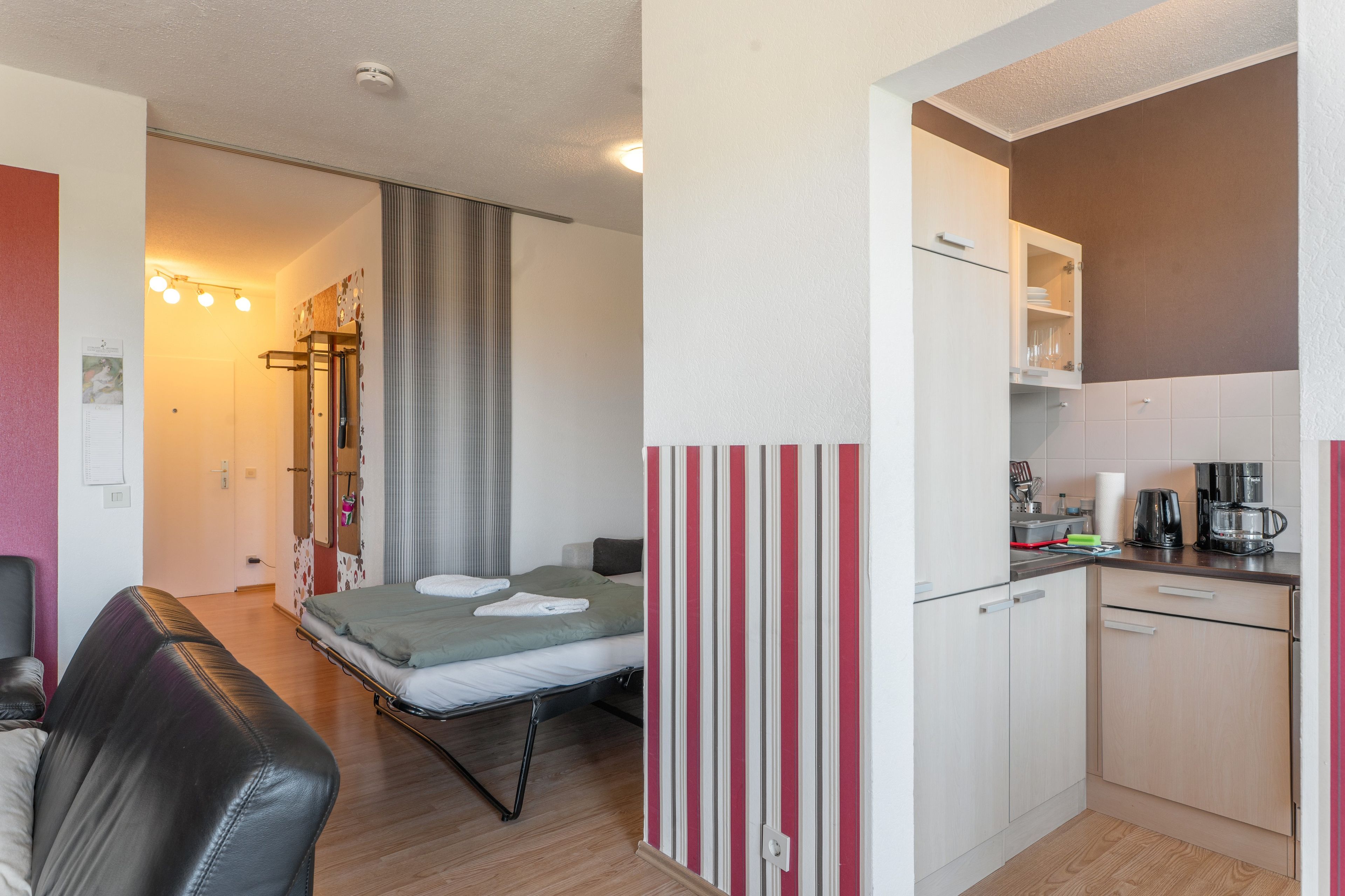 A compact hotel room with a bed, a small kitchenette, a seating area with a couch, and a bathroom with a shower curtain.