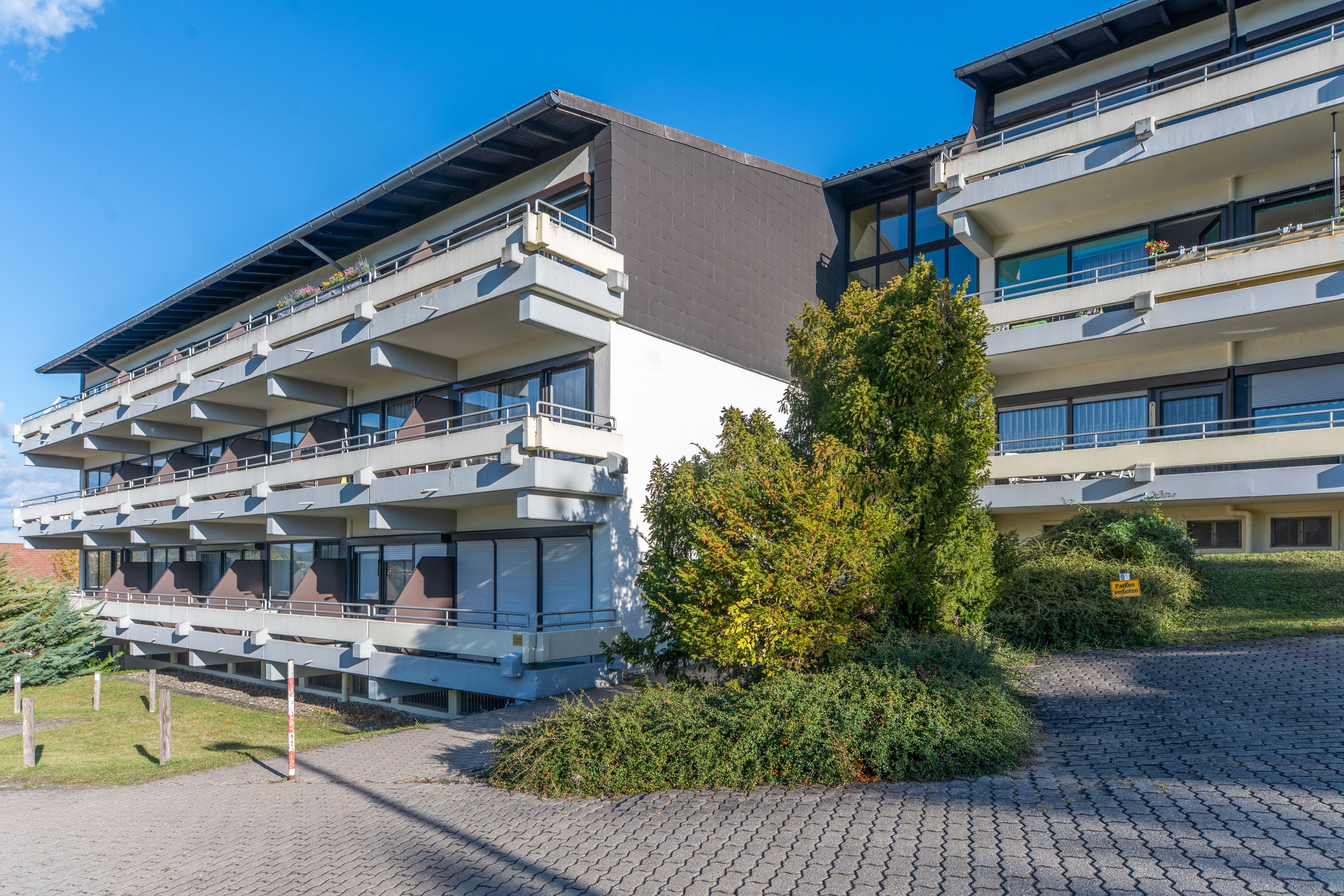 A multi-story building with balconies, a paved courtyard, and a small tree.