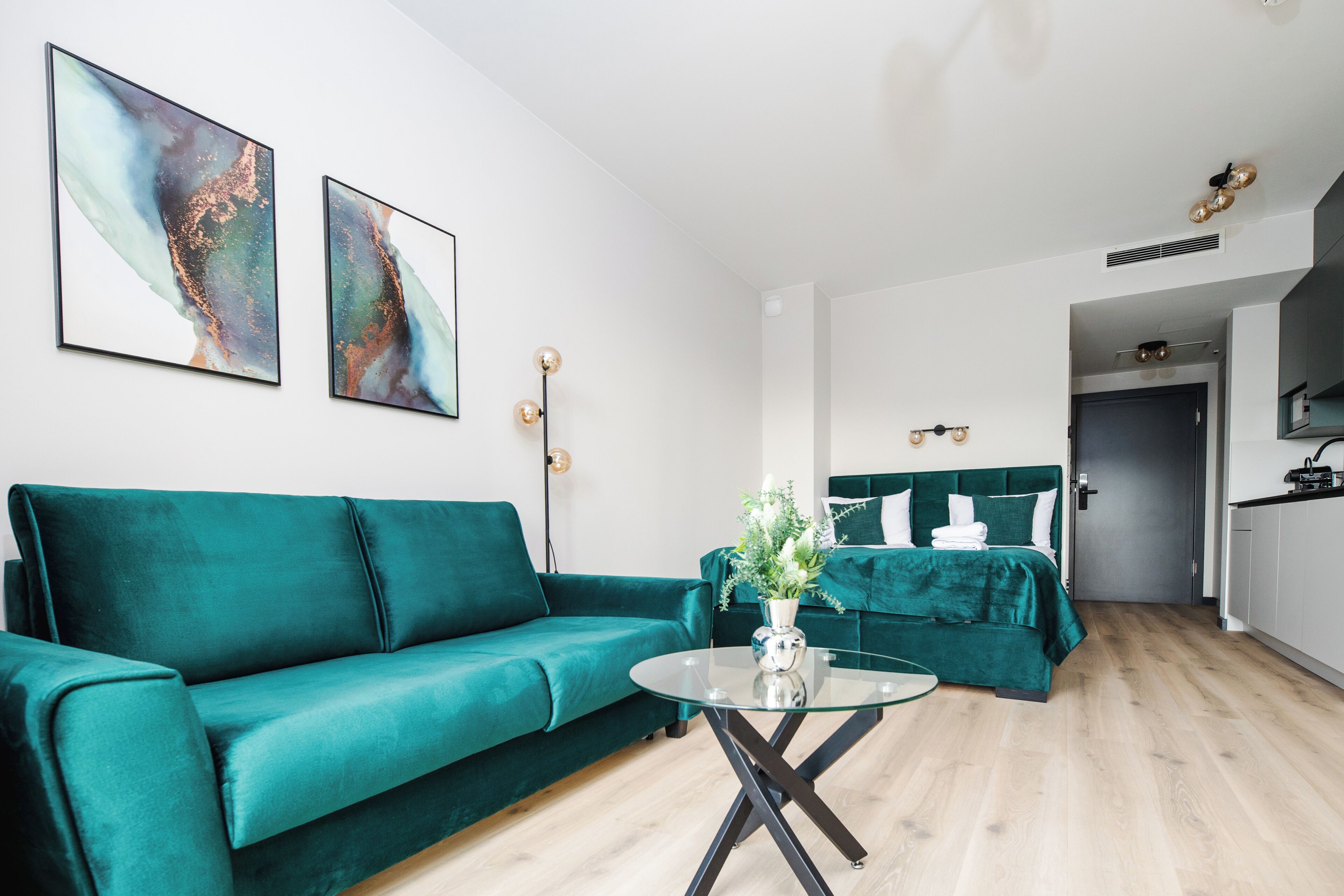 Un salon moderne avec un canapé de couleur turquoise, une table basse en verre et des œuvres d’art abstraites accrochées au mur.
