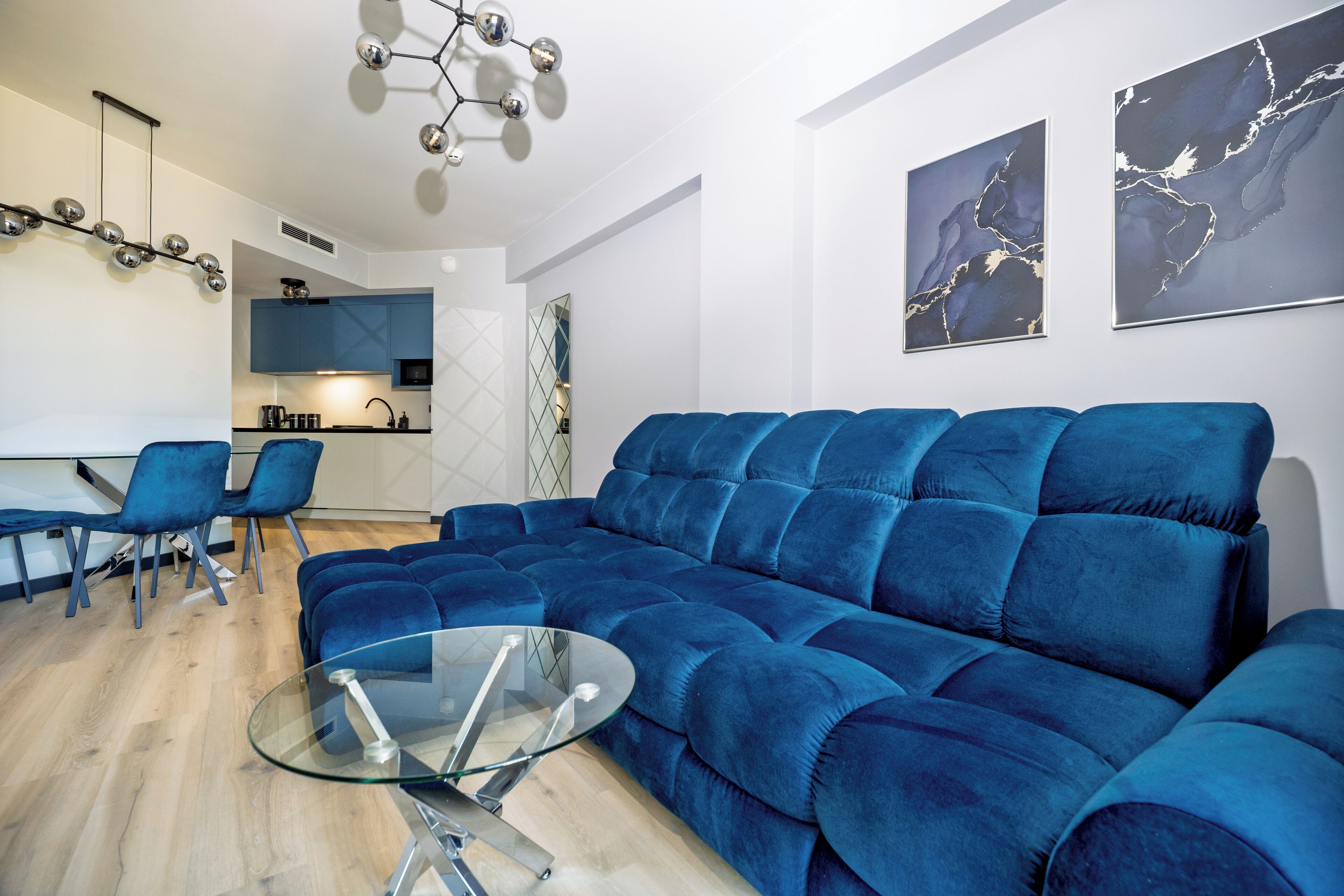 Una sala de estar moderna con un sofá seccional azul, una mesa de centro de vidrio y una zona de comedor con sillas azules.