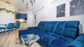 Una sala de estar moderna con un sofá seccional azul, una mesa de centro de vidrio y una zona de comedor con sillas azules.