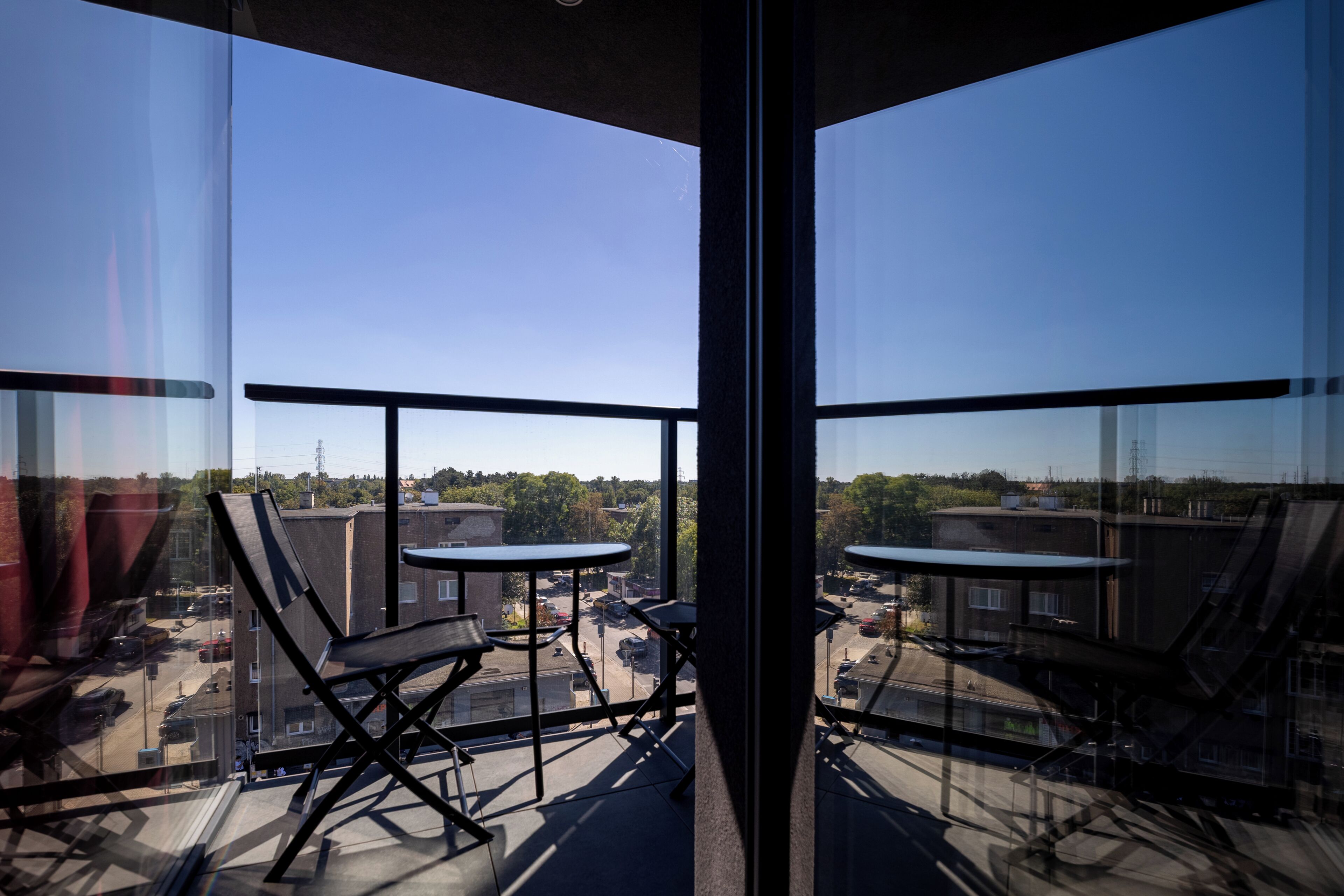 Un balcón con mesa y sillas, con vista a un paisaje urbano de edificios y cielo despejado.