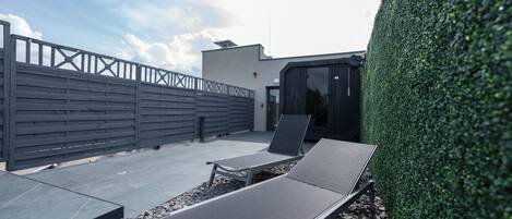 Una terraza en la azotea con dos sillones, un muro bajo y un seto.