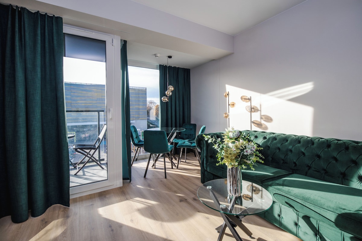 Una sala de estar moderna con un sofá verde, una mesa de centro de cristal y vistas a un paisaje urbano a través de un ventanal grande.
