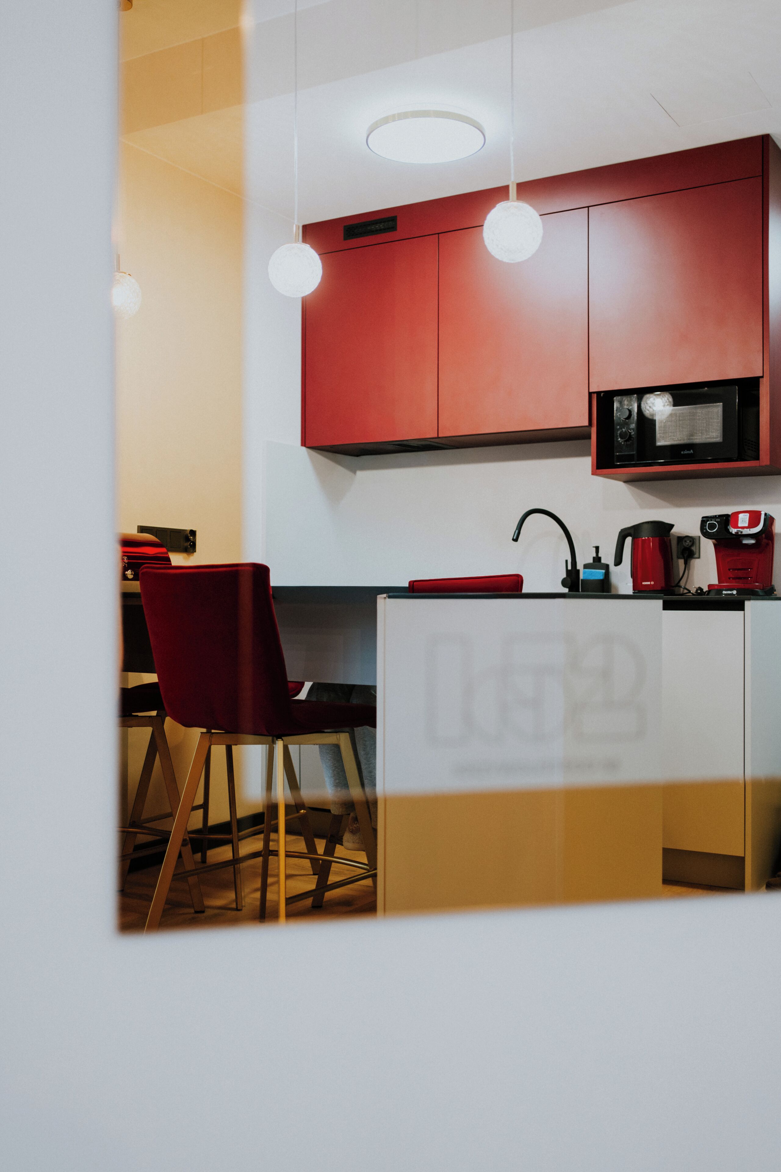 Une cuisine moderne avec des meubles de rangement rouges, un four à micro-ondes, une machine à café et des luminaires suspendus.