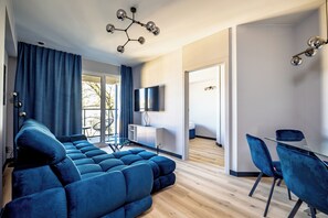 A modern living room with a sectional sofa, a dining area with a glass table and chairs, and a TV mounted on the wall. - K52 Apartments (Wrocław)