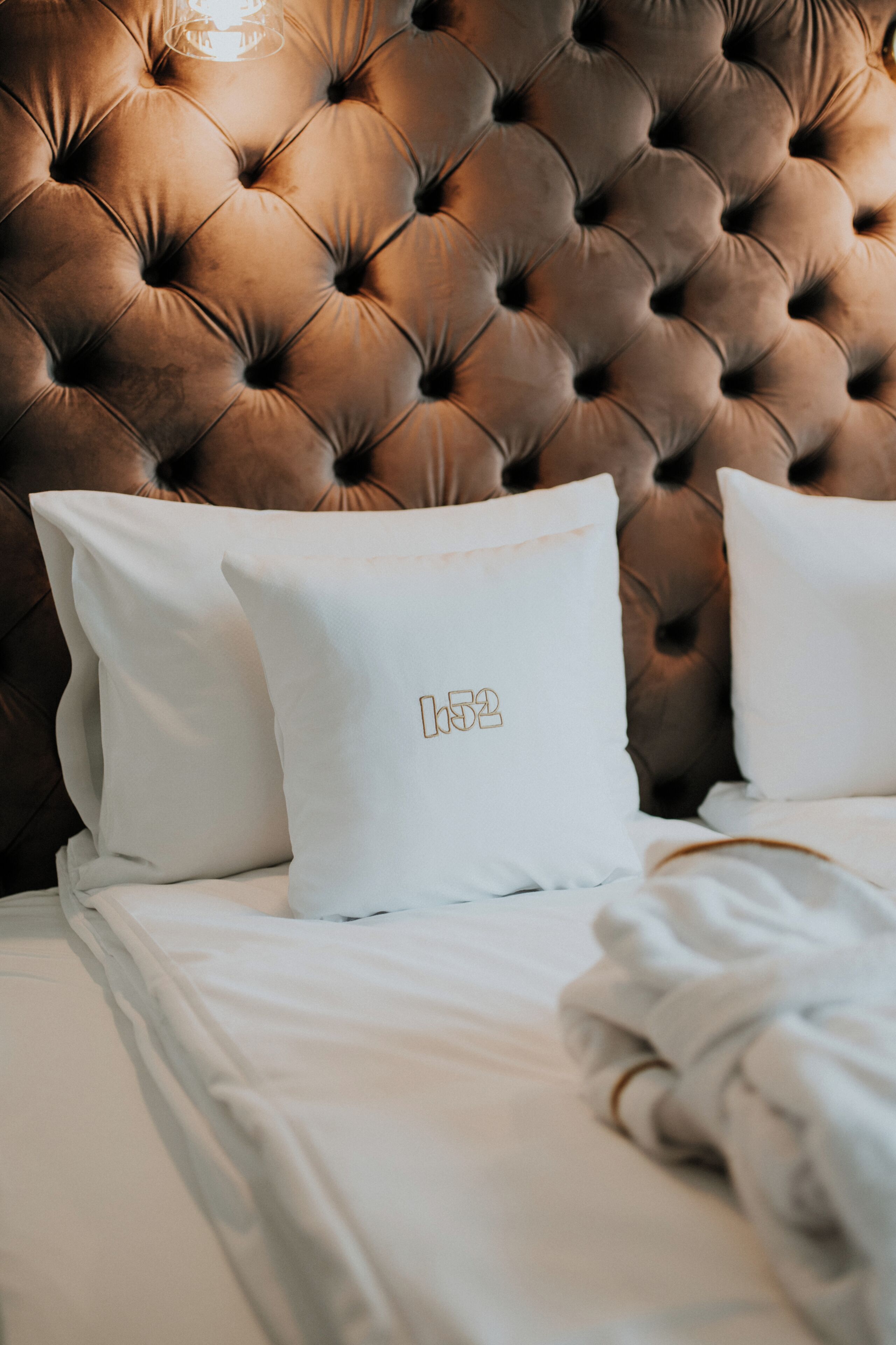 Cama con ropa blanca y dos almohadas con un monograma.
