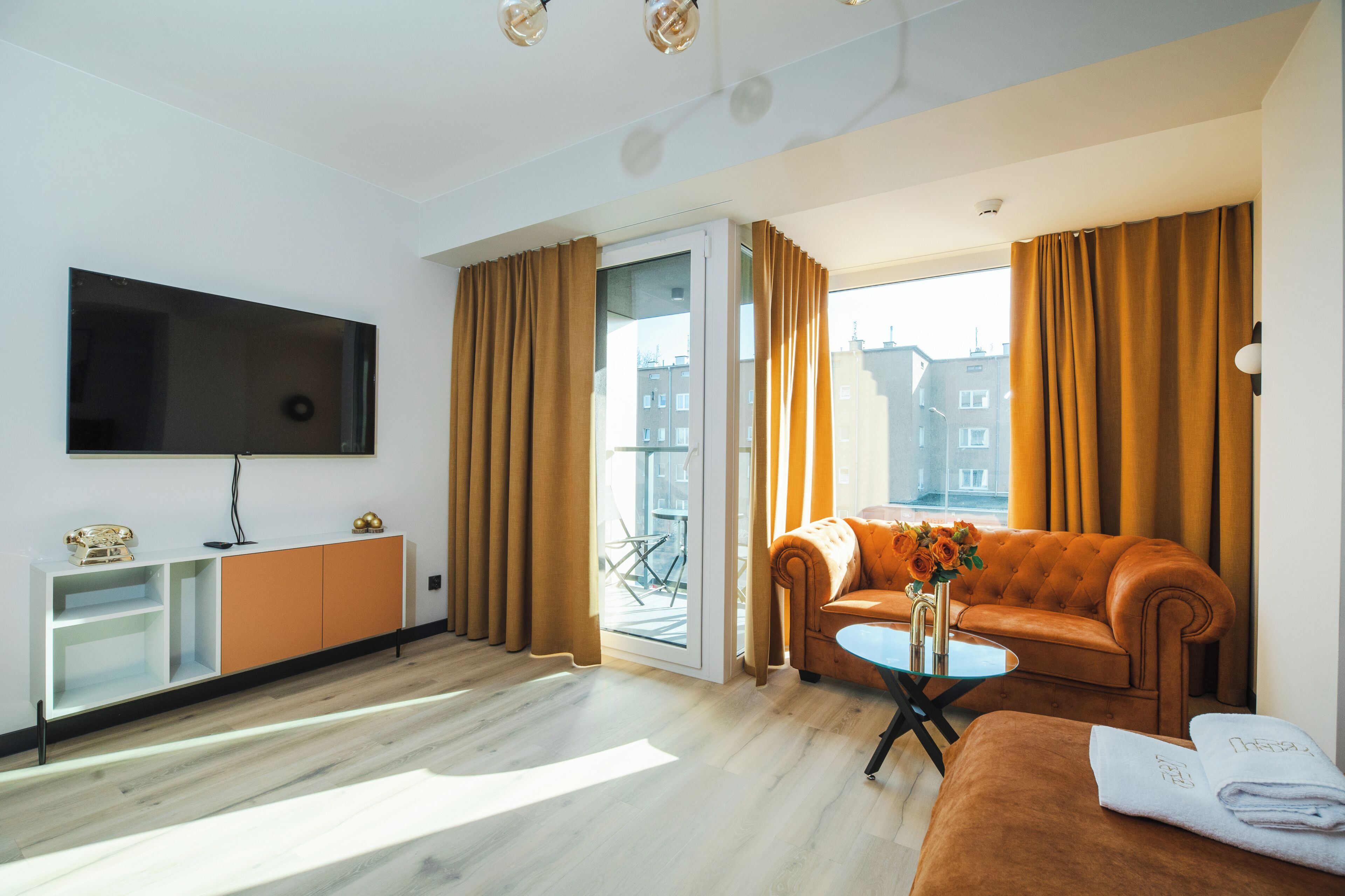 Een moderne woonkamer met een flatscreen televisie, een bank, een salontafel en een uitzicht op de stad door grote ramen.