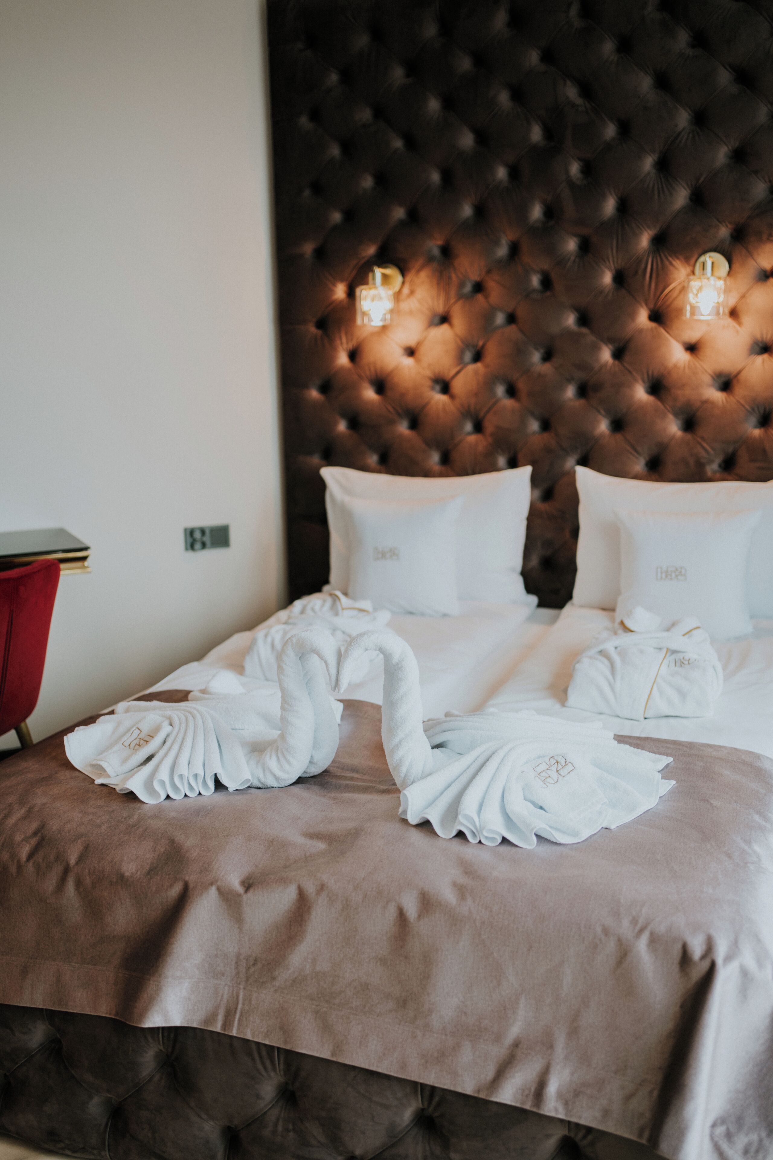 A hotel room with a tufted headboard, a neatly made bed with white linens, and a red side table.