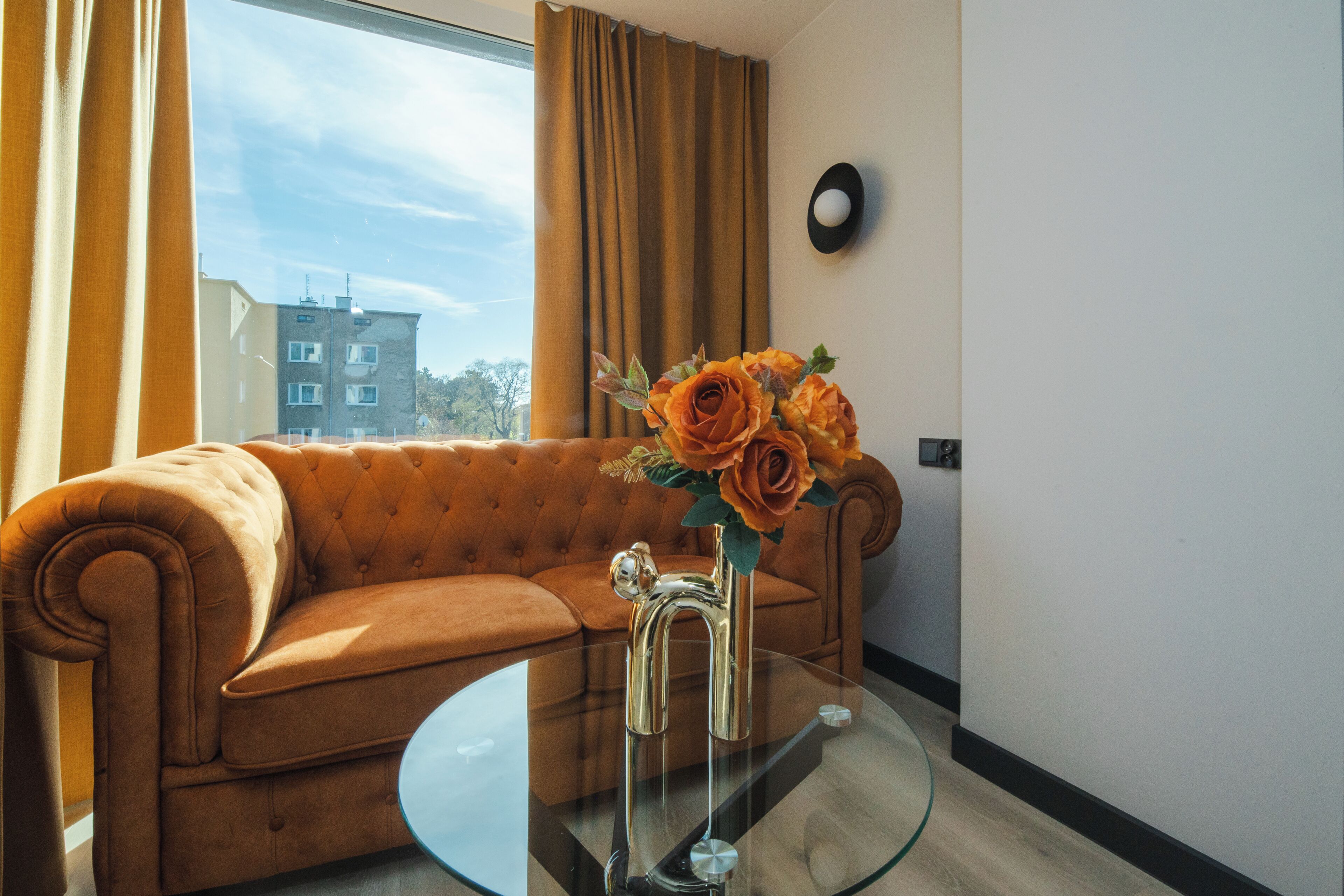 A room with a brown sofa, a glass coffee table, and a vase with flowers.