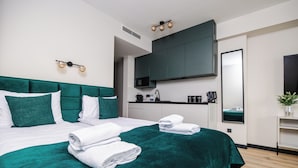 A modern hotel room with a large bed, a flat-screen TV, a coffee machine, and a mirror.