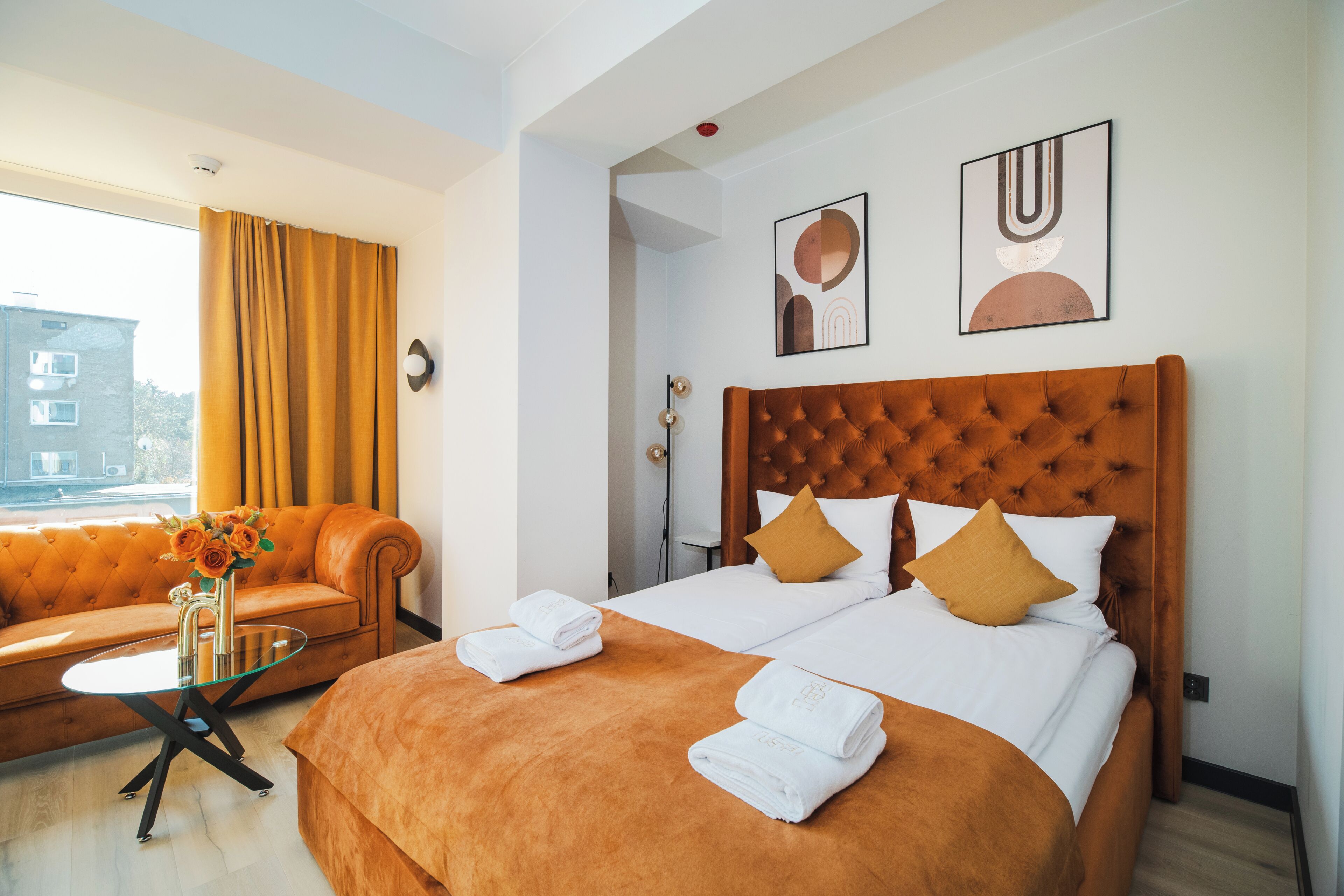 A hotel room with a large bed, a sofa, a small table, and artwork on the walls.