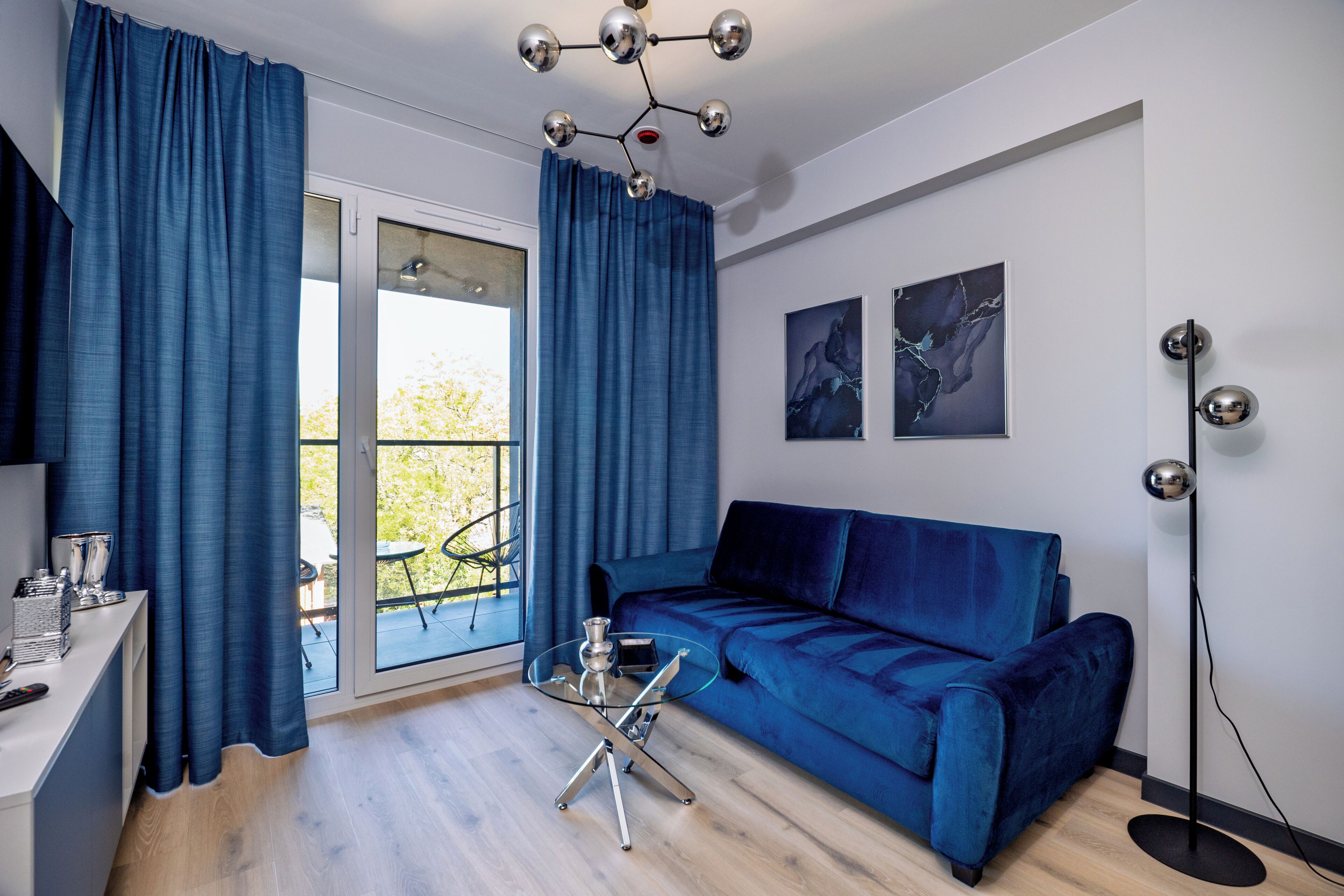 Una sala moderna con un sofá azul, una mesa de centro de vidrio y un comedor con una mesa y sillas blancas.