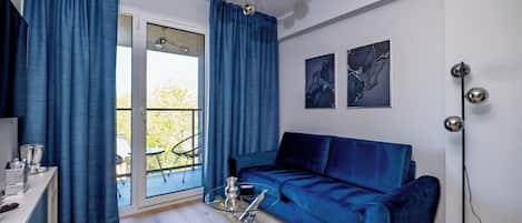Una sala moderna con un sofá azul, una mesa de centro de vidrio y un comedor con una mesa y sillas blancas.