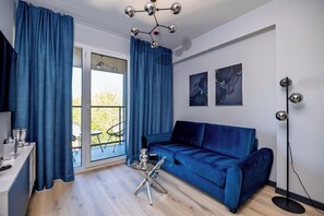 A modern living room with a blue sofa, a glass coffee table, and a dining area with a white table and chairs. - K52 Apartments (Wrocław)