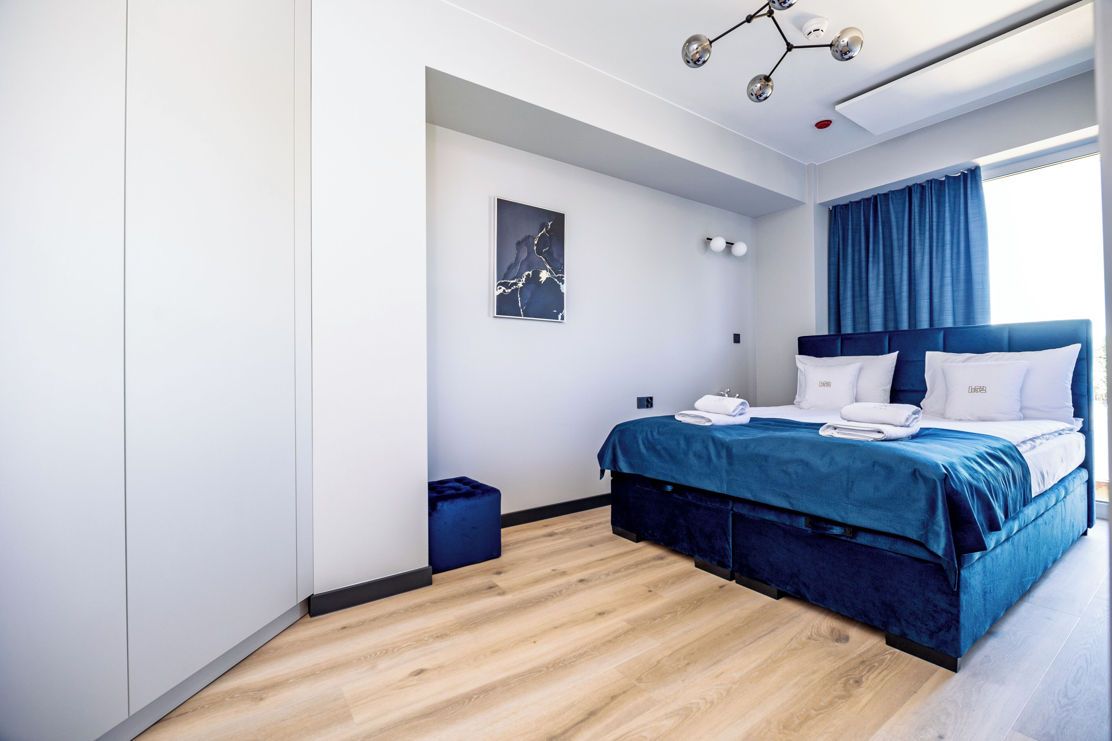 Una habitación de hotel moderna con una cama grande, una mesita de noche, una obra de arte en la pared y una ventana con cortinas.