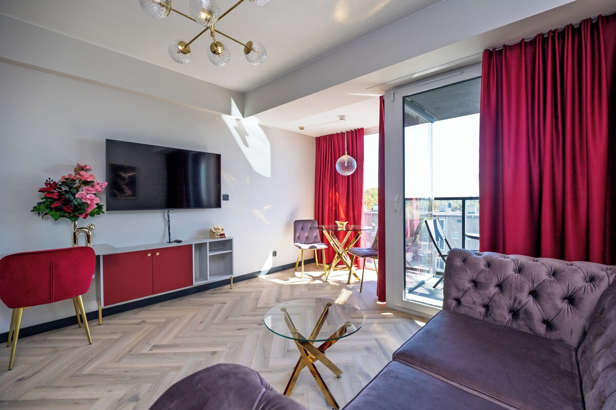 Una sala de estar moderna con un televisor de pantalla plana, muebles rojos y una mesa de centro de vidrio.