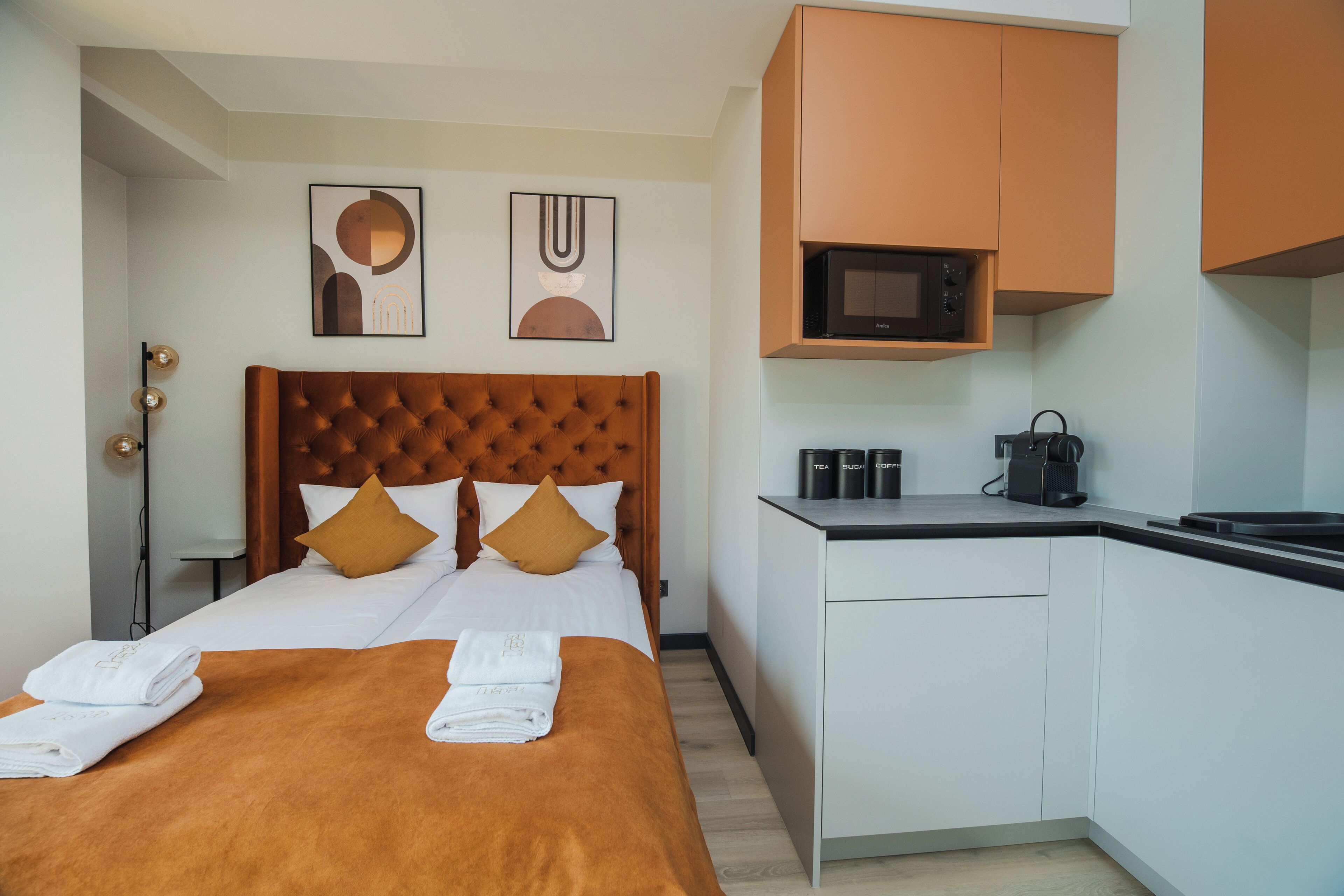 A hotel room with a bed, a kitchenette, and two wall-mounted artworks.