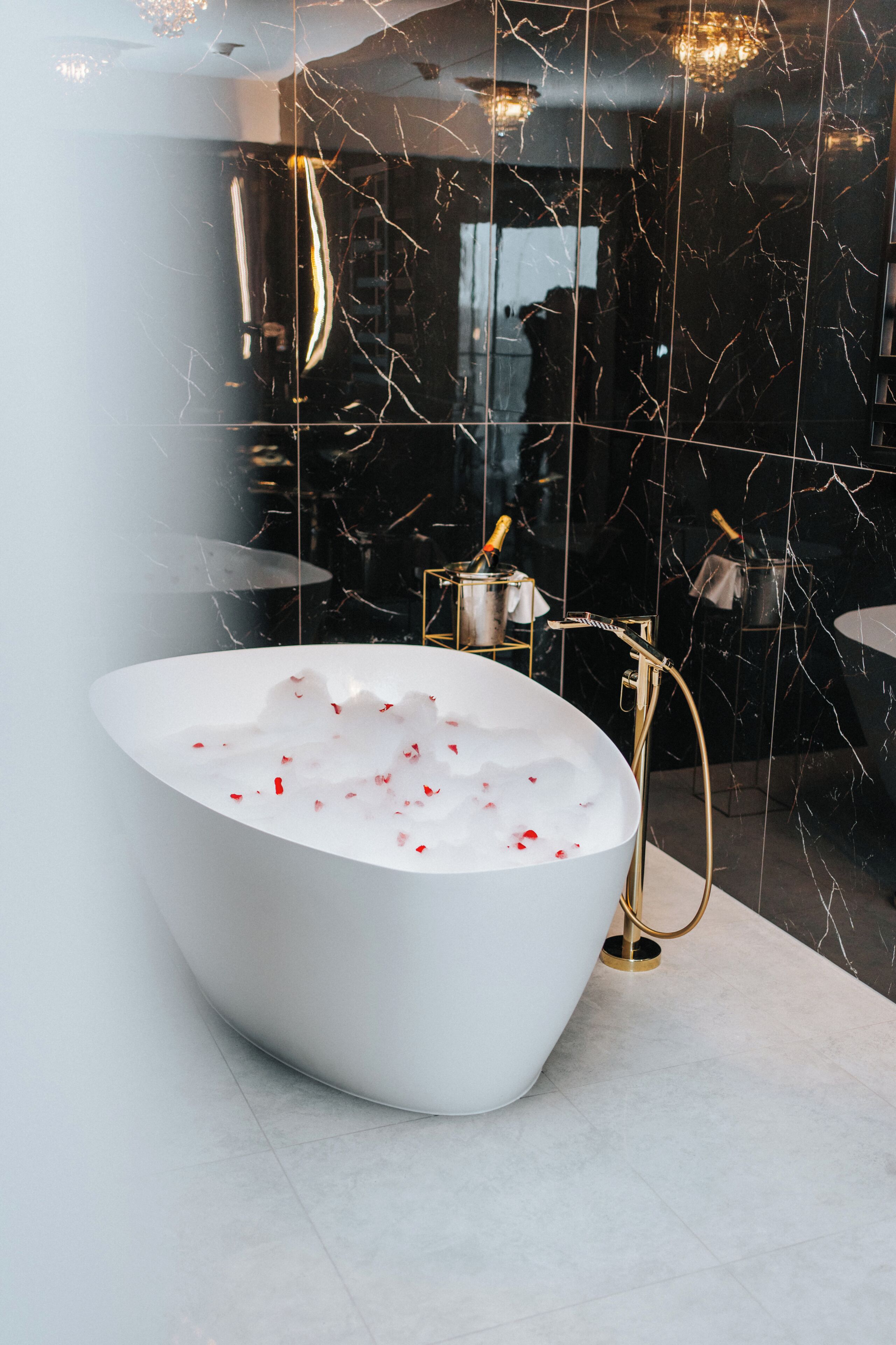 A modern bathroom with a freestanding bathtub, a gold-colored faucet, and a marble wall with visible cracks.