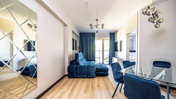 Habitación de hotel moderna con un amplio sofá modular, una mesa de comedor de cristal y una pared espejada.