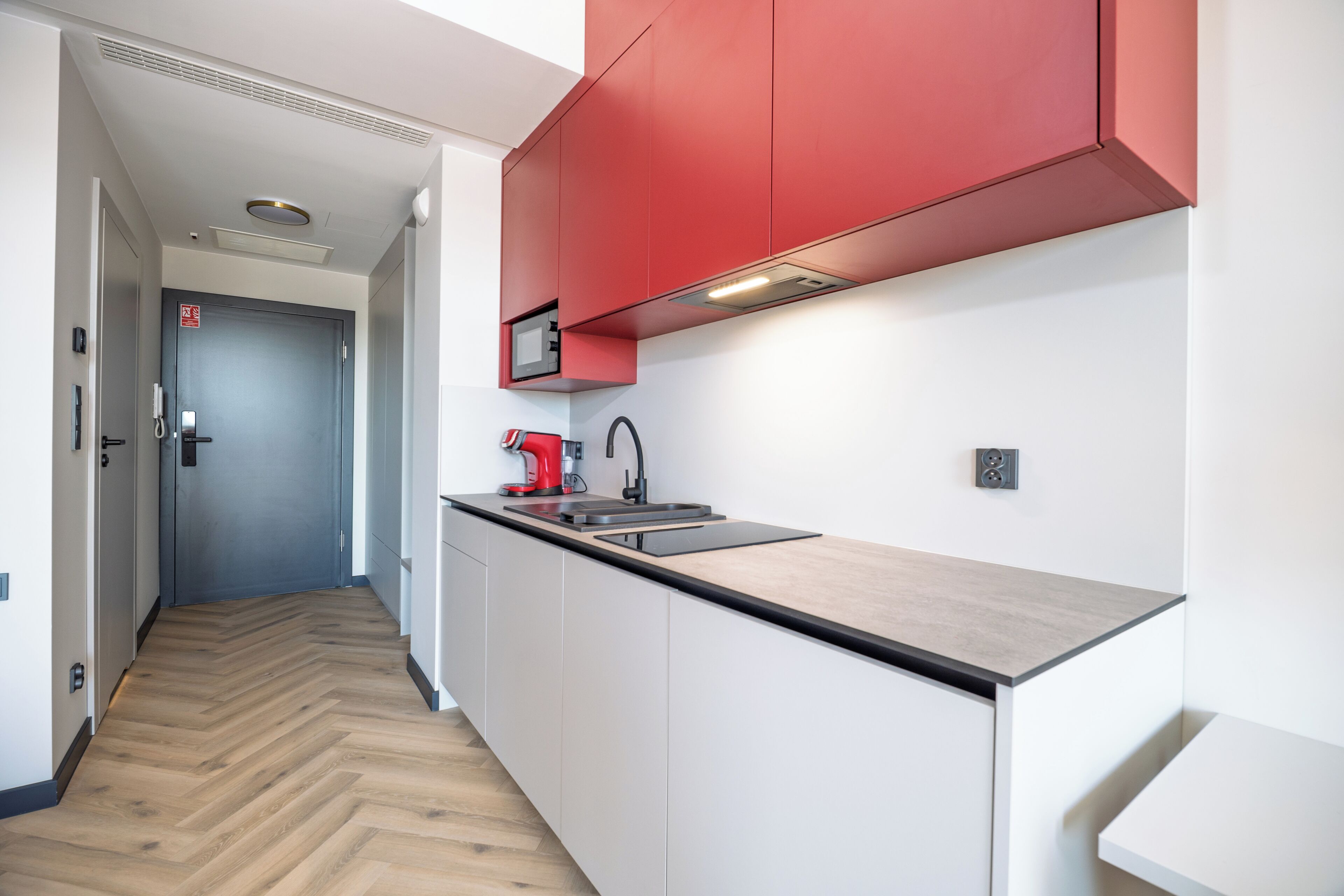 A modern kitchen with a herringbone wood floor, white cabinetry, and red accents.