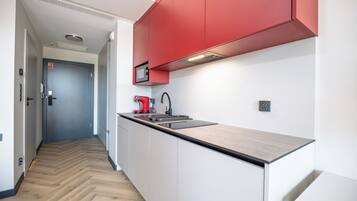 A modern kitchen with a herringbone wood floor, white cabinetry, and red accents.