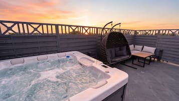 Ein Whirlpool auf einer Dachterrasse mit Holzzaun, einem Korbschaukelstuhl und einem Tisch mit Kissen.