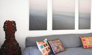 A grey sofa with colorful pillows and a wall with three abstract paintings. - A two-bedroom villa with saltwater swimming pool, sun terrace, BBQ and gardens (Corralejo)