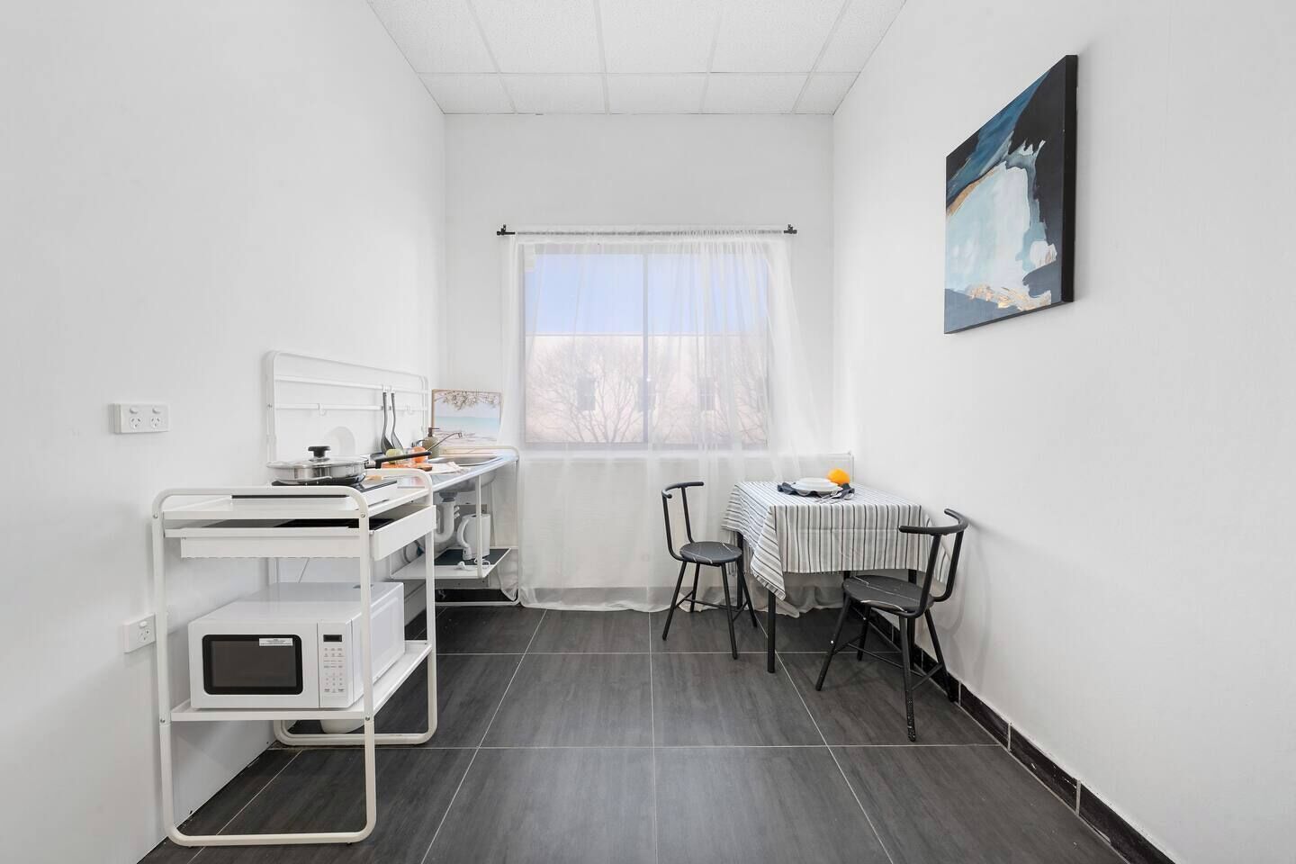 A small, clean room with a desk, chair, and a window with sheer curtains.