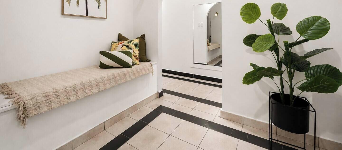 A hallway with a bench, a potted plant, and a mirror.