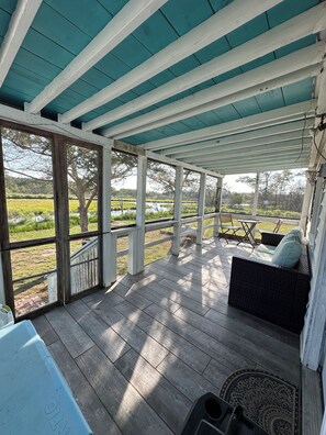 A covered porch with a view of a grassy field and a body of water.