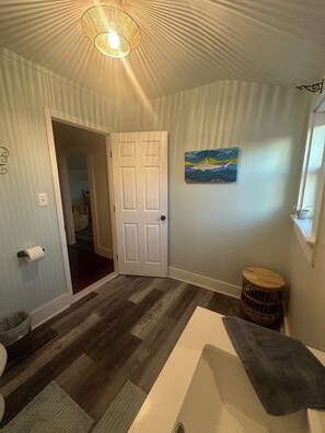 Una habitación con piso estampado, una puerta que da a otra habitación, un cuadro en la pared y un taburete pequeño y redondo.