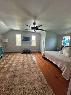 A bedroom with a bed, a ceiling fan, two windows, a rug, and a painting. - Red Fish Riviera - A low country charmer on the backwaters of the Pamlico Sound. (Engelhard)