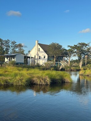Une maison avec un grand jardin à l’avant et un plan d’eau devant.