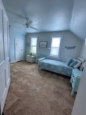 Un dormitorio con cama, mesita de noche, cómoda, ventilador de techo, ventanas y decoración en la pared.