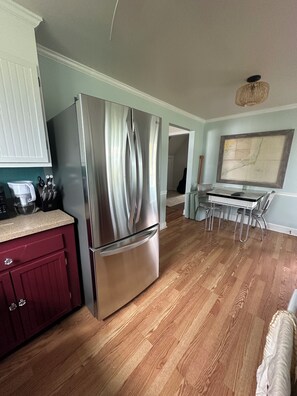 Une cuisine équipée d’un réfrigérateur en acier inoxydable, d’un plancher en bois, d’une table à manger avec des chaises et d’un grand tableau encadré accroché au mur.