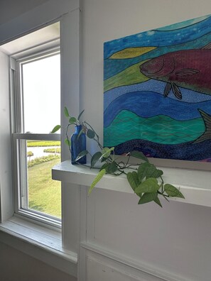 Una habitación con una ventana, un cuadro de un pez y una planta en un estante.