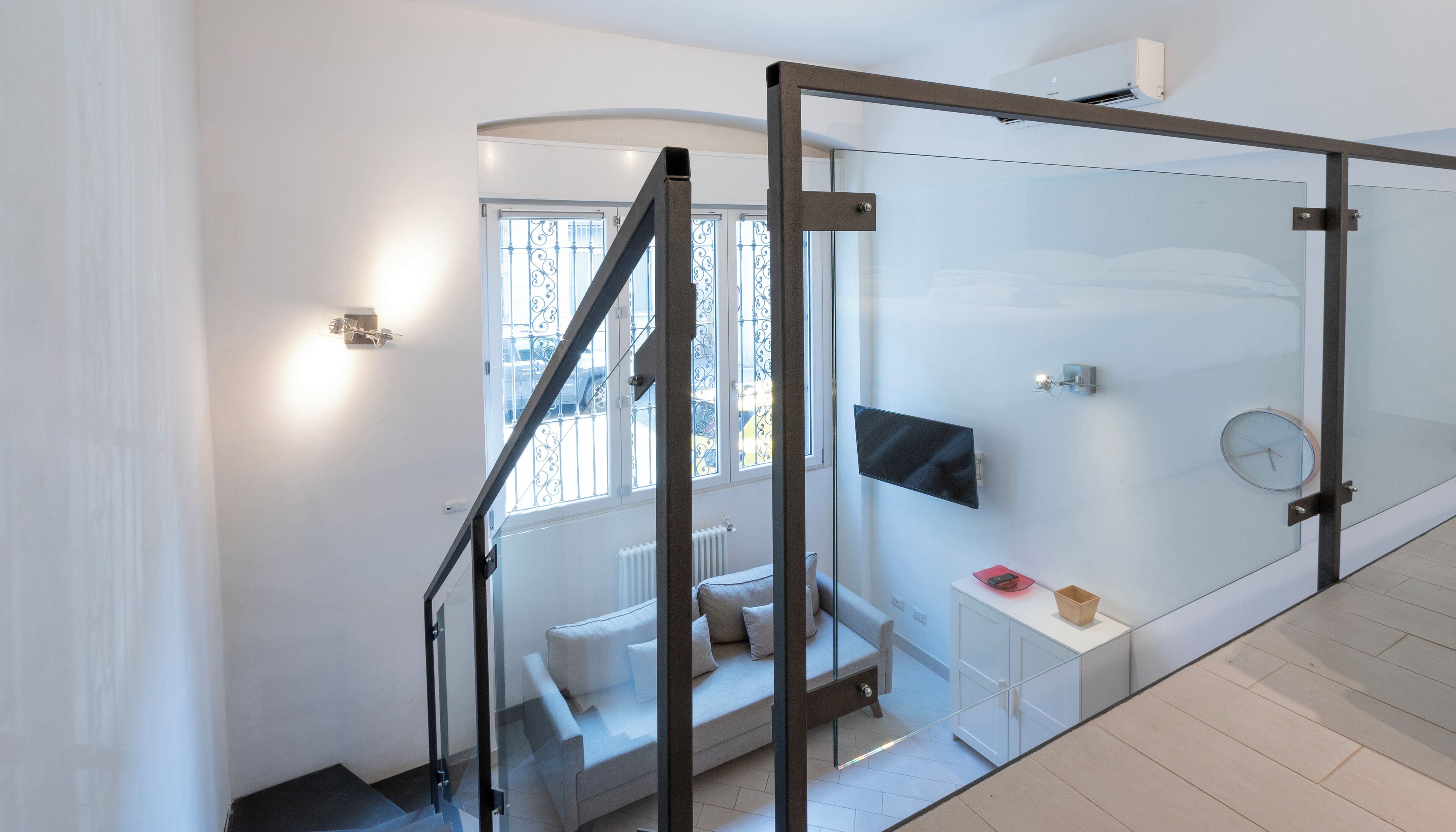 Un interior moderno con una escalera, un sofá, un televisor y un reloj.