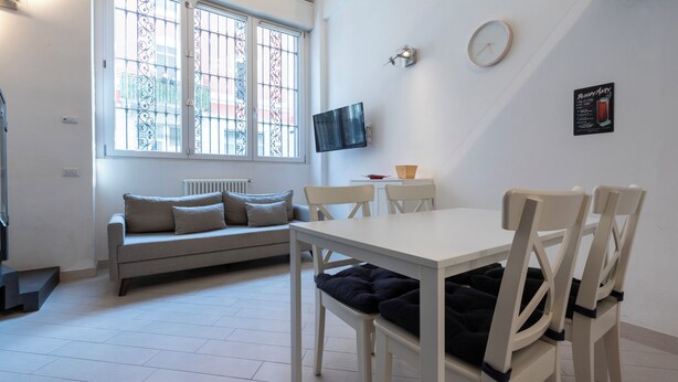 A modern living room with a sofa, a dining table, chairs, a TV, and a window with bars.