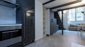 A modern kitchen with built-in appliances, a staircase leading to a balcony, and a dining area with a table and chairs.