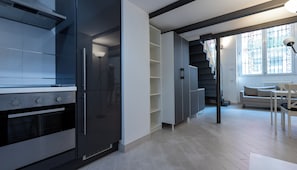 A modern kitchen with built-in appliances, a staircase leading to a balcony, and a dining area with a table and chairs. - Italianway Easy - Verro 46 (Milan)
