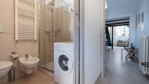 A modern bathroom with a glass shower enclosure, a washing machine, and a bidet.