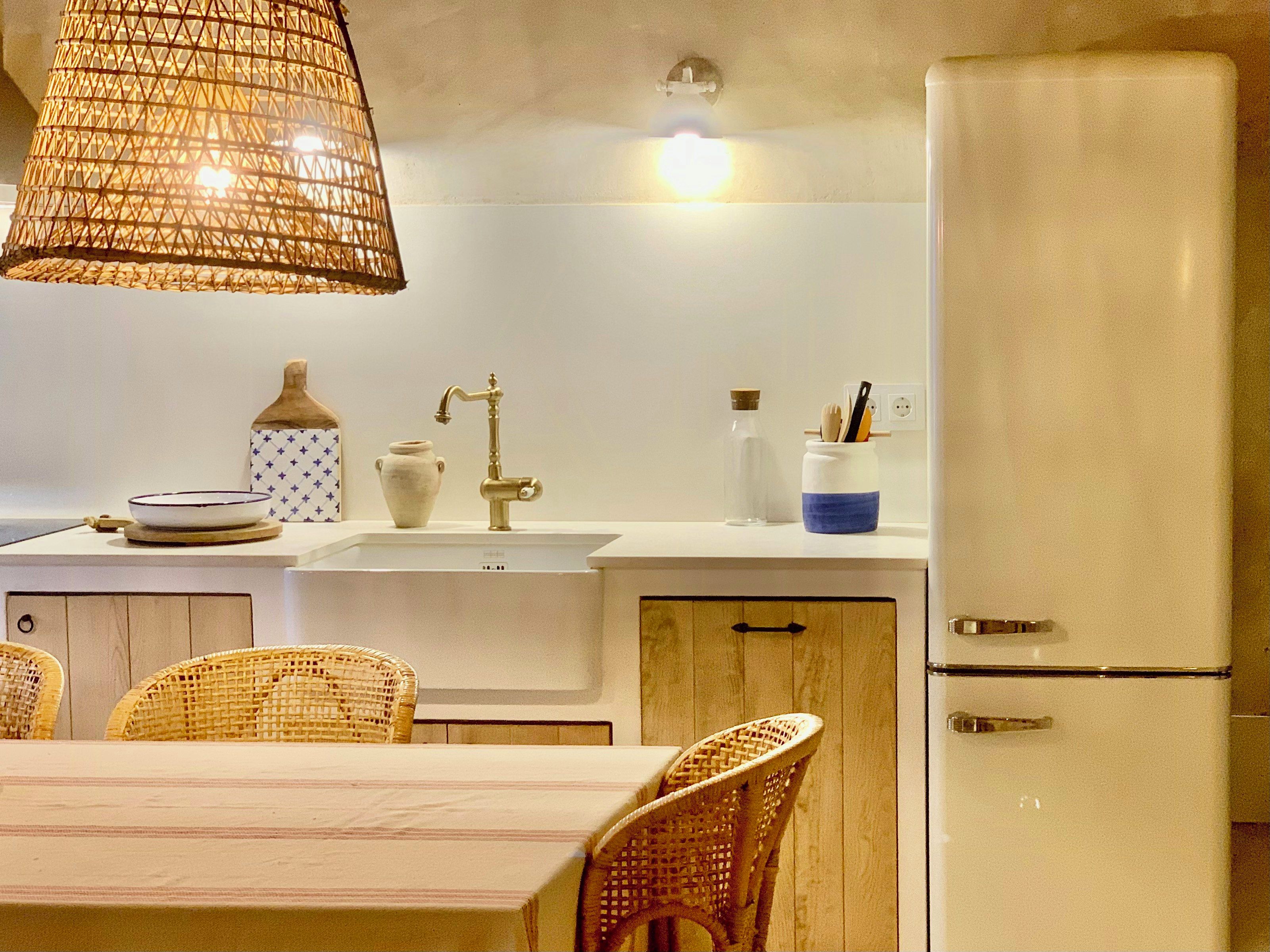 A kitchen with a white refrigerator, a sink, a dining table with chairs, and a hanging light fixture.