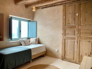 A bedroom with a bed, a window with blue shutters, a wooden wardrobe, and a hanging light fixture. - Restored fisherman's house in l'Escala (L'Escala)