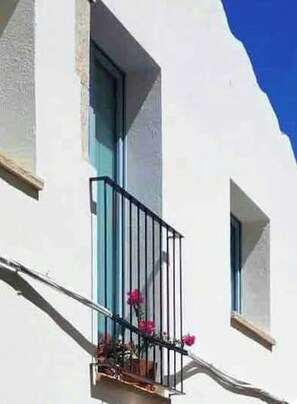 Ein weißes Gebäude mit einem Balkon, der ein Metallgitter und Kübel mit rosa Blumen zeigt.