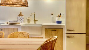 A kitchen with a white countertop, a sink, a stainless steel refrigerator, wicker chairs, and a hanging light fixture. - Restored fisherman's house in l'Escala (L'Escala)