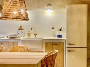 A kitchen with a white countertop, a sink, a stainless steel refrigerator, wicker chairs, and a hanging light fixture. - Restored fisherman's house in l'Escala (L'Escala)