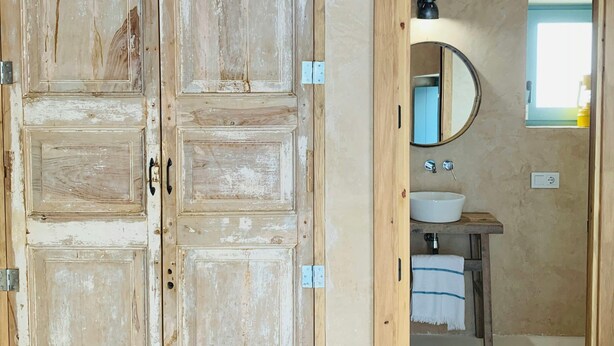 A rustic bathroom with a wooden door, a round mirror, and a white sink. - Restored fisherman's house in l'Escala (L'Escala)